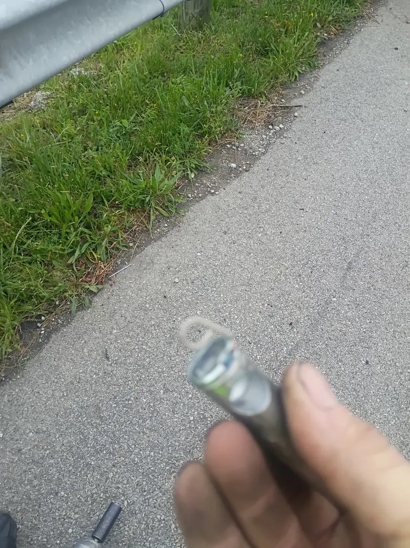 Technician holding a lug socket beside a highway shoulder where a nail sits in the pavement next to the guardrail