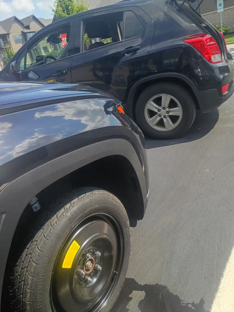 Temporary compact spare donut tire installed on the front of an SUV in a parking lot