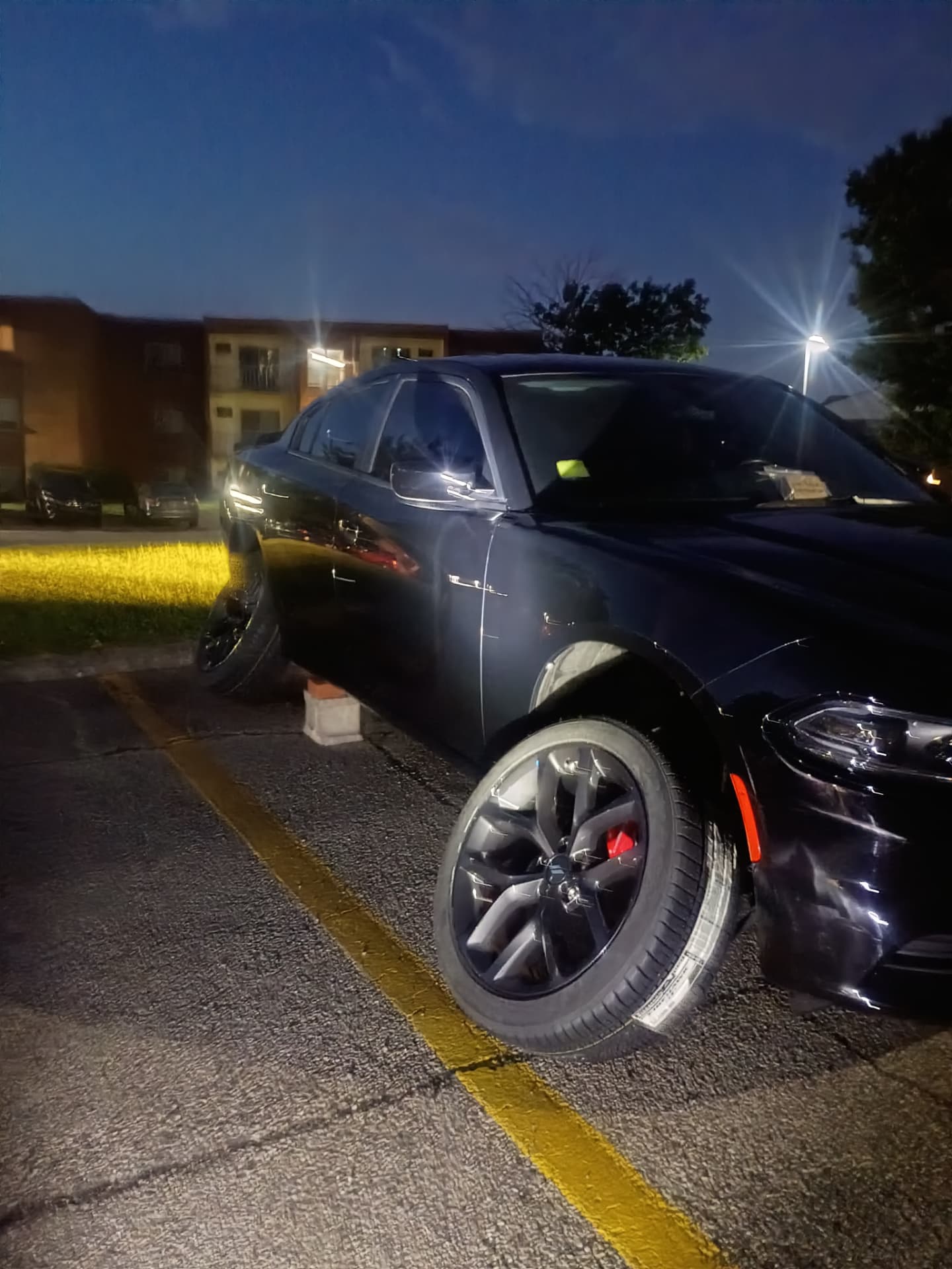 Dodge Charger lifted on a jack stand at night in a lit parking lot during an after-hours mobile tire change