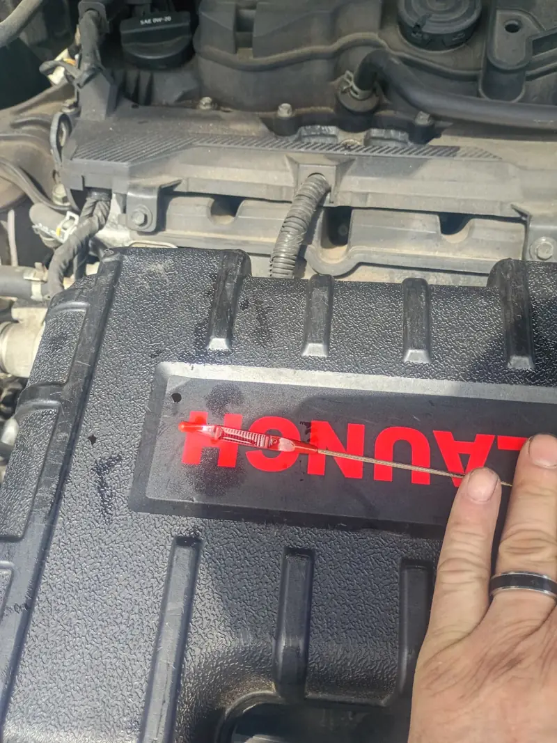 Technician holding an engine oil dipstick above the engine cover while checking fluid level during a roadside visit