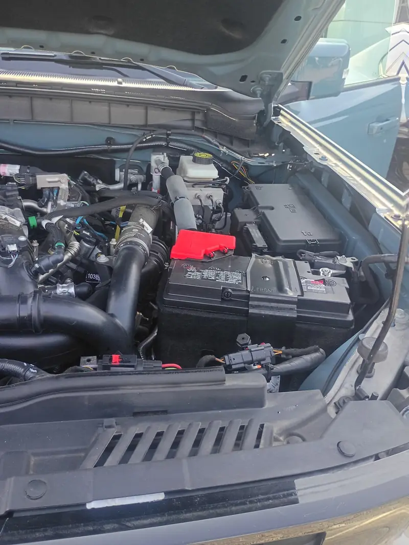 Open engine bay of a pickup truck showing the battery and terminals during a roadside jump start