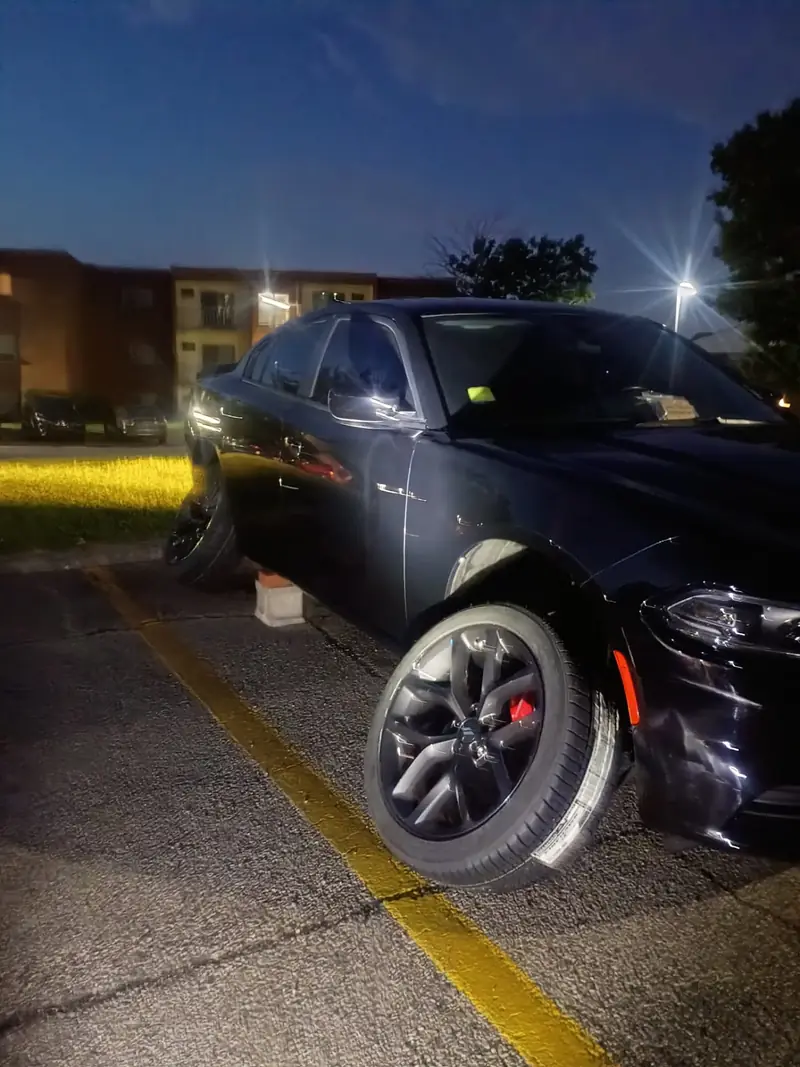 Dodge Charger lifted on a jack stand at night in a lit parking lot during an after-hours mobile tire change