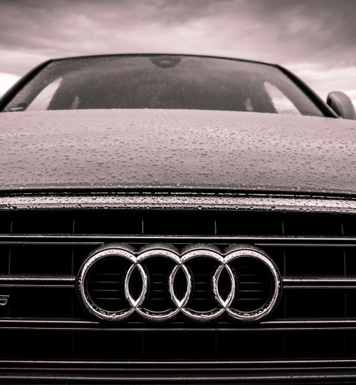 Close-up of a rain-covered Audi car grille showcasing luxury and elegance under cloudy skies.