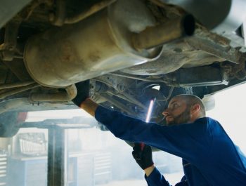 Skilled mechanic performing thorough maintenance under a vehicle in a professional garage setting.