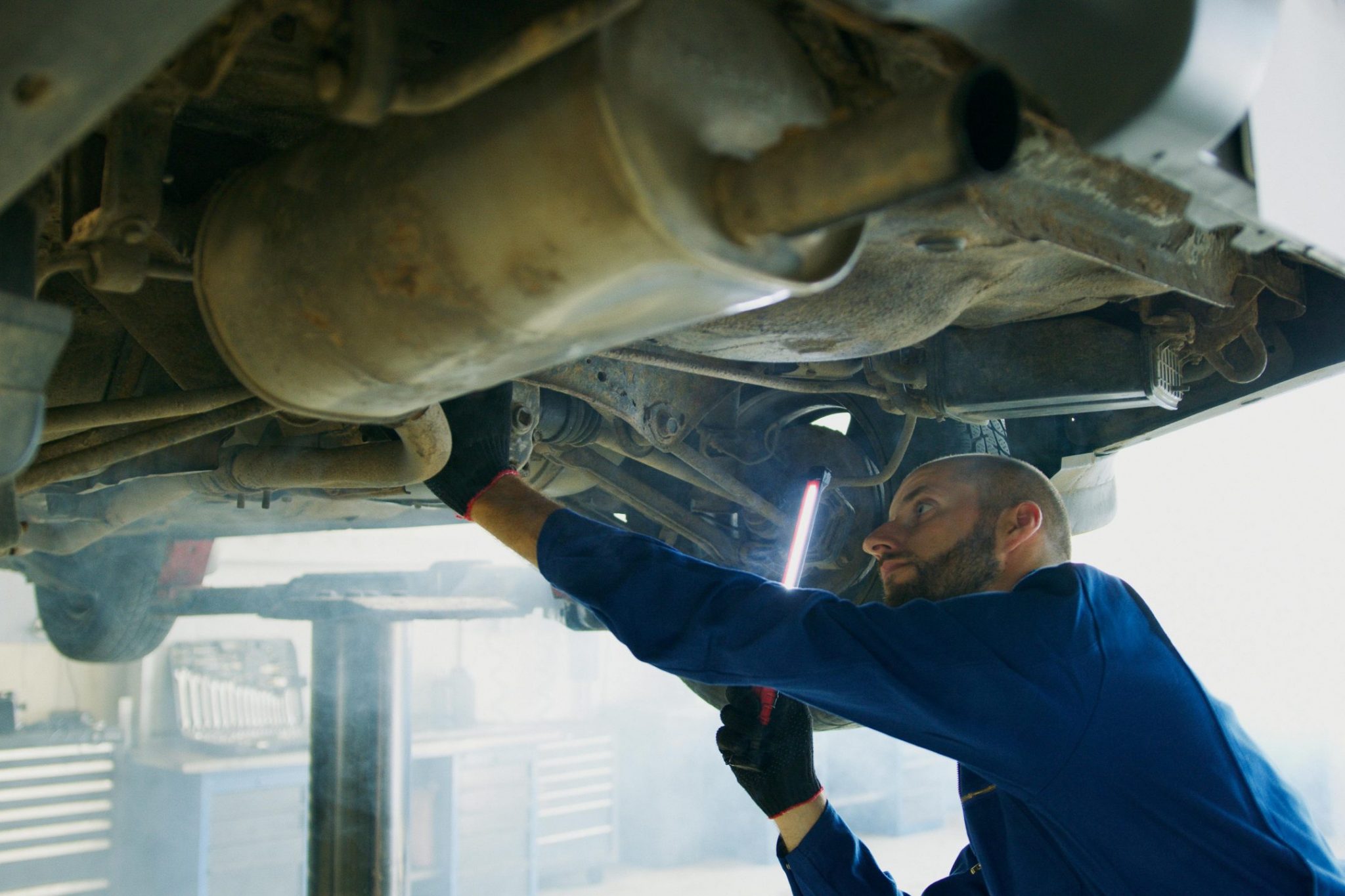Skilled mechanic performing thorough maintenance under a vehicle in a professional garage setting.